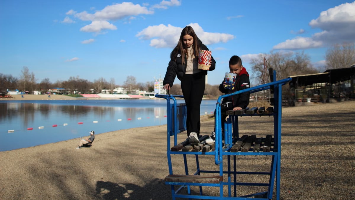 Two kids with popcorn by a lake, enjoying a sunny autumn day.